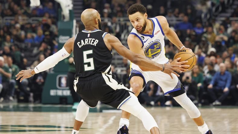 Dec 13, 2022; Milwaukee, Wisconsin, USA; Golden State Warriors guard Stephen Curry (30) holds the ball away from Milwaukee Bucks guard Jevon Carter (5) during the first quarter at Fiserv Forum. Mandatory Credit: Jeff Hanisch-USA TODAY Sports