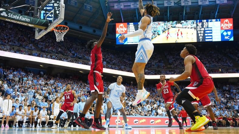 Jan 21, 2023; Chapel Hill, North Carolina, USA; North Carolina Tar Heels guard R.J. Davis (4) shoots as North Carolina State Wolfpack forward Ebenezer Dowuona (21) and guard LJ Thomas (4) defend in the second half at Dean E. Smith Center. Mandatory Credit: Bob Donnan-USA TODAY Sports
