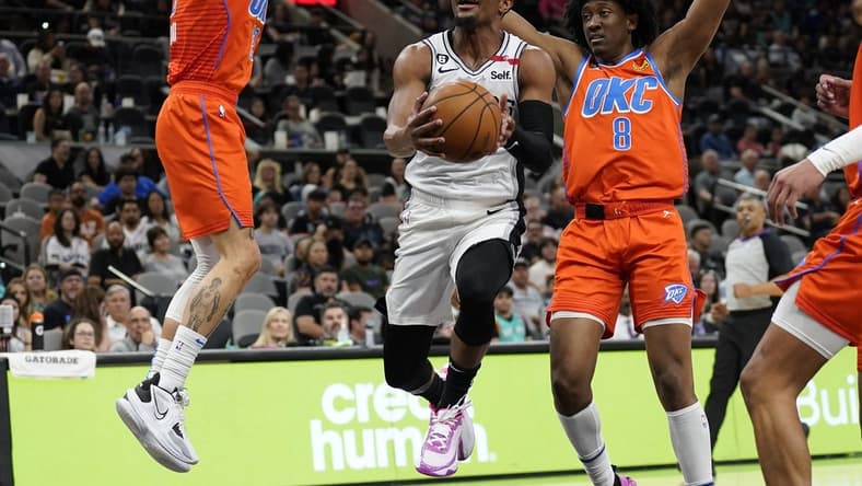 Mar 12, 2023; San Antonio, Texas, USA; San Antonio Spurs guard Devonte' Graham (4) drives to the basket between Oklahoma City Thunder guard Josh Giddey (3) and forward Jalen Williams (8) during the first half at AT&T Center. Mandatory Credit: Scott Wachter-USA TODAY Sports