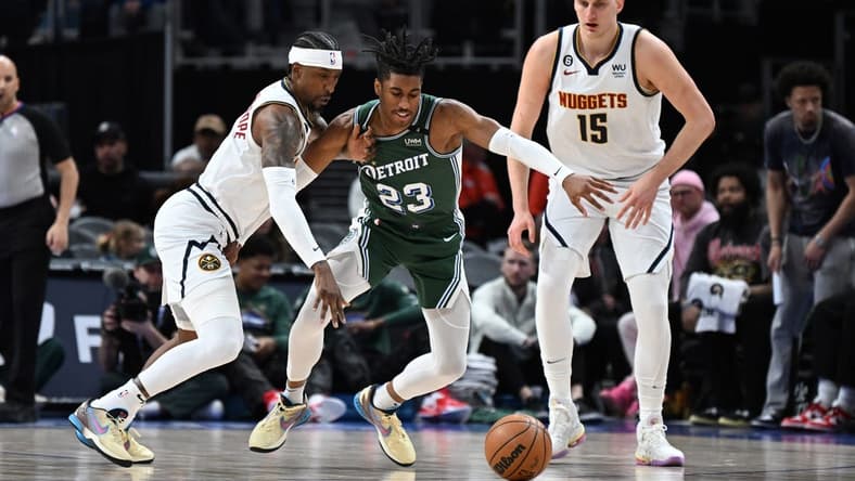 Mar 16, 2023; Detroit, Michigan, USA; Denver Nuggets guard Kentavious Caldwell-Pope (5) (left) knocks the ball away from Detroit Pistons guard Jaden Ivey (23) as Denver Nuggets center Nikola Jokic (15) watches in the first quarter at Little Caesars Arena. Mandatory Credit: Lon Horwedel-USA TODAY Sports