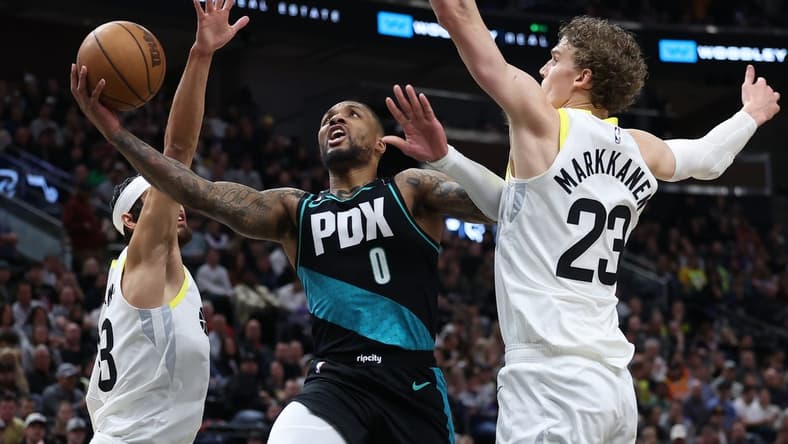 Mar 22, 2023; Salt Lake City, Utah, USA; Portland Trail Blazers guard Damian Lillard (0) drives between Utah Jazz guard Johnny Juzang (33) and forward Lauri Markkanen (23) in the second quarter at Vivint Arena. Mandatory Credit: Rob Gray-USA TODAY Sports