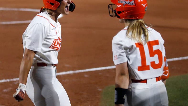 Oklahoma State's Kiley Naomi (5) celebrates a score with Rachel Becker (15) in the first inning during a softball game between Oklahoma State and Utah in the Women's College World Series at USA Softball Hall of Fame Stadium in in Oklahoma City, Friday, June, 2, 2023.