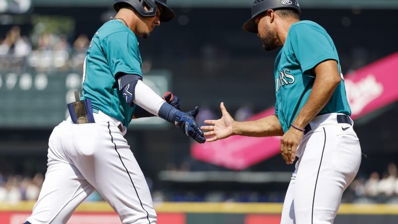 Aug 28, 2023; Seattle, Washington, USA; Seattle Mariners second baseman Josh Rojas (4, left) shakes hands with first base coach Kristopher Negr n (45) after hitting a solo-home run against the Kansas City Royals during the third inning at T-Mobile Park. Mandatory Credit: Joe Nicholson-USA TODAY Sports