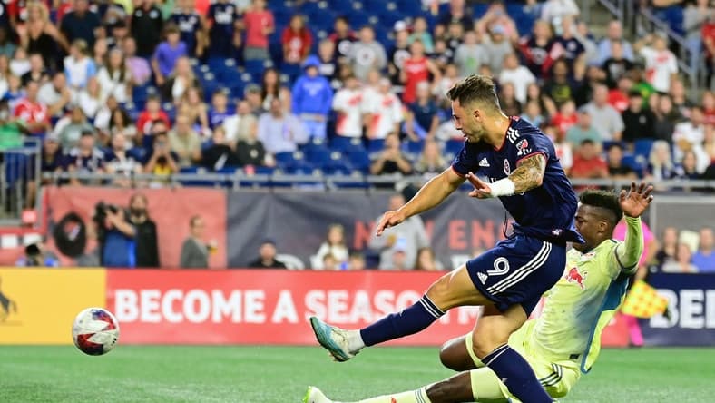 Aug 30, 2023; Foxborough, Massachusetts, USA; New England Revolution attacker Giacomo Vrioni (9) scores a goal as New York Red Bulls defender Hassan Ndam (98) slides to defend the shot during the first half at Gillette Stadium. Mandatory Credit: Eric Canha-USA TODAY Sports