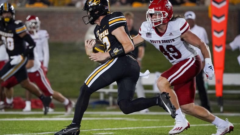 Aug 31, 2023; Columbia, Missouri, USA; Missouri Tigers quarterback Brady Cook (12) runs the ball as South Dakota Coyotes linebacker Brock Mogensen (49) defends during the first half at Faurot Field at Memorial Stadium. Mandatory Credit: Denny Medley-USA TODAY Sports