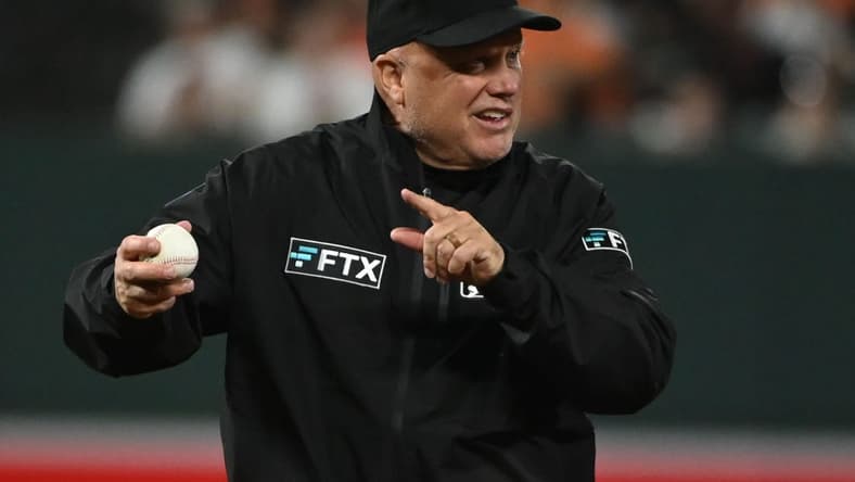 Apr 12, 2022; Baltimore, Maryland, USA;  Umpire Brian O'Nora (7) signals while holding a baseball during the game between the Baltimore Orioles and the Milwaukee Brewers at Oriole Park at Camden Yards. Mandatory Credit: Tommy Gilligan-USA TODAY Sports