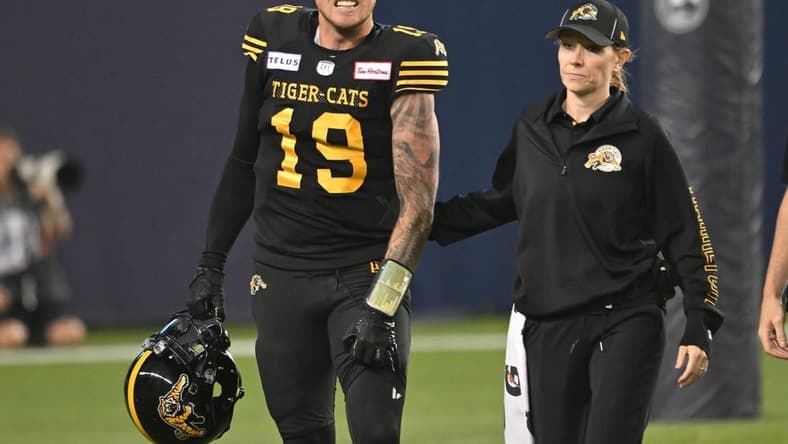 Jun 18, 2023; Toronto, Ontario, CAN; Hamilton Tiger-Cats quarterback Bo Levi Mitchell (19) is escorted off the field by team head therapist Claire Tofflemire after suffering an injury against the Toronto Argonauts in the fourth quarter at BMO Field. Mandatory Credit: Dan Hamilton-USA TODAY Sports