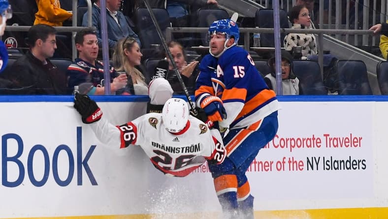 Oct 26, 2023; Elmont, New York, USA; New York Islanders right wing Cal Clutterbuck (15) checks Ottawa Senators defenseman Erik Brannstrom (26) into the boards during the second period at UBS Arena. Mandatory Credit: Dennis Schneidler-USA TODAY Sports