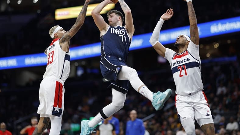 Nov 15, 2023; Washington, District of Columbia, USA; Dallas Mavericks guard Luka Doncic (77) leaps to pass the ball as Washington Wizards forward Kyle Kuzma (33) and Wizards center Daniel Gafford (21) defend in the first quarter at Capital One Arena. Mandatory Credit: Geoff Burke-USA TODAY Sports