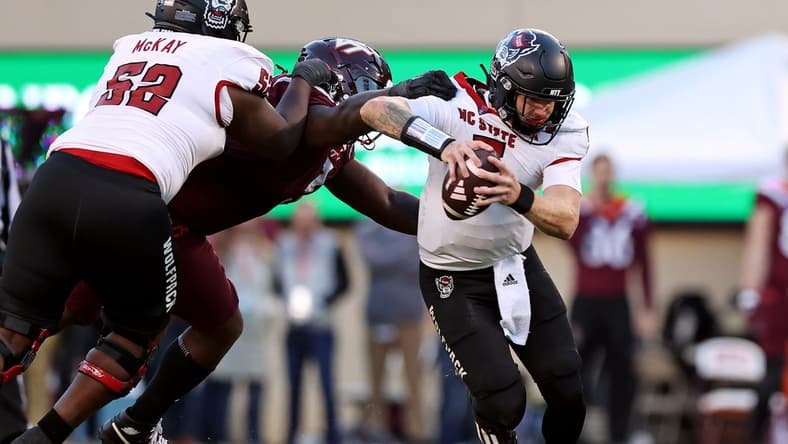 Nov 18, 2023; Blacksburg, Virginia, USA; North Carolina State Wolfpack quarterback Brennan Armstrong (5) runs from Virginia Tech Hokies defensive lineman Norell Pollard (3) during the second quarter at Lane Stadium. Mandatory Credit: Peter Casey-USA TODAY Sports
