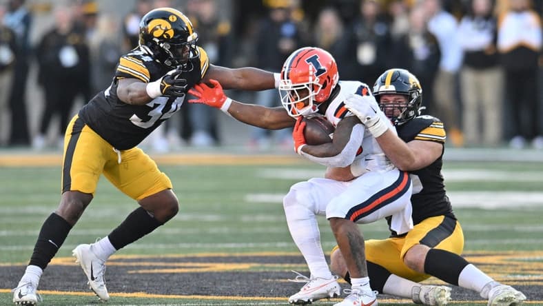 Nov 18, 2023; Iowa City, Iowa, USA; Illinois Fighting Illini running back Reggie Love III (23) is tackled by Iowa Hawkeyes defensive lineman Logan Lee (85) and linebacker Jay Higgins (34) during the second quarter at Kinnick Stadium. Mandatory Credit: Jeffrey Becker-USA TODAY Sports