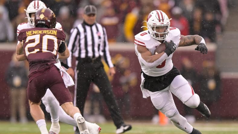 Nov 25, 2023; Minneapolis, Minnesota, USA; Wisconsin Badgers running back Braelon Allen (0) runs with the ball as quarterback Tanner Mordecai (8) puts a block on Minnesota Golden Gophers defensive back Jack Henderson (20) at Huntington Bank Stadium. Mandatory Credit: Nick Wosika-USA TODAY Sports