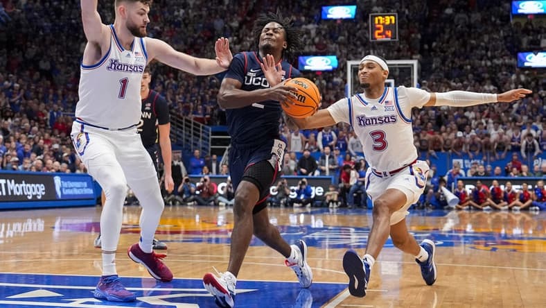 Dec 1, 2023; Lawrence, Kansas, USA; Connecticut Huskies guard Tristen Newton (2) drives against Kansas Jayhawks center Hunter Dickinson (1) and guard Dajuan Harris Jr. (3) during the first half at Allen Fieldhouse. Mandatory Credit: Jay Biggerstaff-USA TODAY Sports