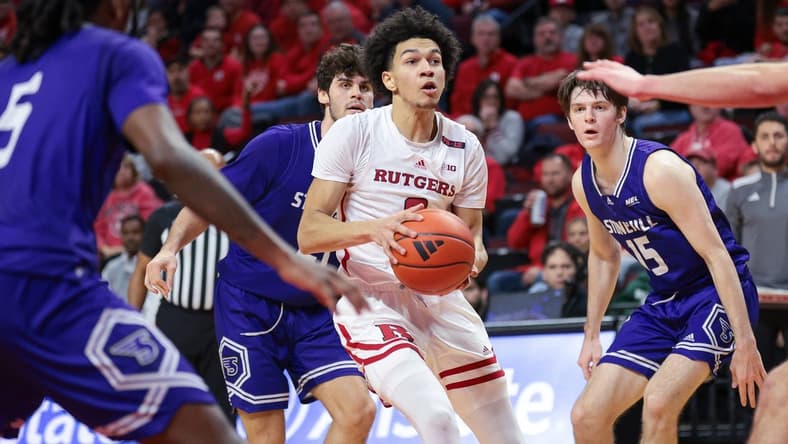 Dec 30, 2023; Piscataway, New Jersey, USA; Rutgers Scarlet Knights guard Derek Simpson (0) drives to the basket in front of Stonehill Skyhawks guard Josh Mack (5) and guard John O'Reilly III (15) during the first half at Jersey Mike's Arena. Mandatory Credit: Vincent Carchietta-USA TODAY Sports