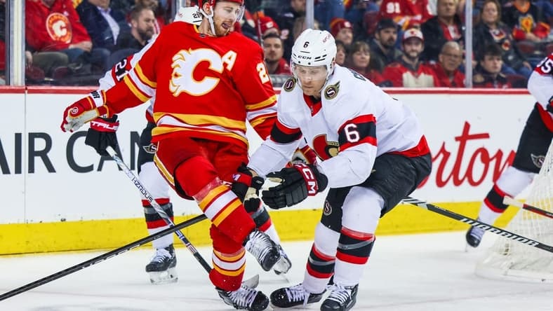 Jan 9, 2024; Calgary, Alberta, CAN; Calgary Flames center Elias Lindholm (28) passes the puck with his skate against Ottawa Senators defenseman Jakob Chychrun (6) during the second period at Scotiabank Saddledome. Mandatory Credit: Sergei Belski-USA TODAY Sports
