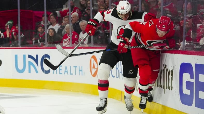 May 3, 2023; Raleigh, North Carolina, USA; New Jersey Devils defenseman Ryan Graves (33) checks Carolina Hurricanes right wing Jesse Puljujarvi (13) during the third period in game one of the second round of the 2023 Stanley Cup Playoffs at PNC Arena. Mandatory Credit: James Guillory-USA TODAY Sports