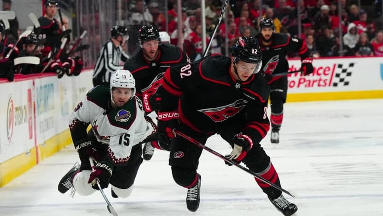 Jan 27, 2024; Raleigh, North Carolina, USA; Carolina Hurricanes center Jesperi Kotkaniemi (82) skates with the puck past Arizona Coyotes center Alexander Kerfoot (15) during the third period at PNC Arena. Mandatory Credit: James Guillory-USA TODAY Sports