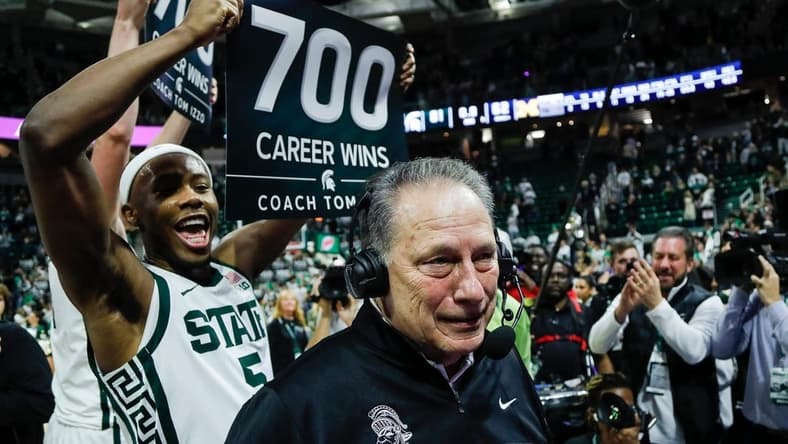 Michigan State guard Tre Holloman (5) holds a sign celebrating 700 career wins as head coach Tom Izzo is being interviewed after MSU's 81-62 win over Michigan at Breslin Center in East Lansing on Tuesday, Jan. 30, 2024.