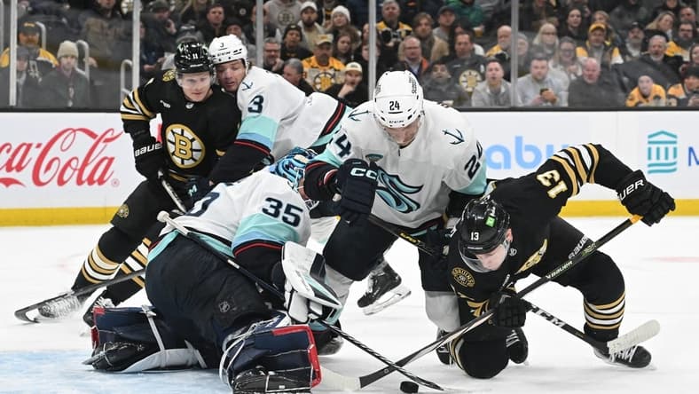 Feb 15, 2024; Boston, Massachusetts, USA; Boston Bruins center Charlie Coyle (13) battles for the puck against Seattle Kraken goaltender Joey Daccord (35) and defenseman Jamie Oleksiak (24) during the first period at TD Garden. Mandatory Credit: Brian Fluharty-USA TODAY Sports