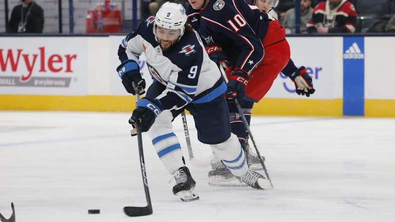 Mar 17, 2024; Columbus, Ohio, USA; Winnipeg Jets left wing Alex Iafallo (9) passes the puck as Columbus Blue Jackets left wing Dmitri Voronkov (10) trails the play during the first period at Nationwide Arena. Mandatory Credit: Russell LaBounty-USA TODAY Sports