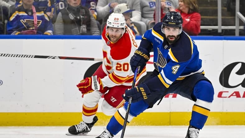 Mar 28, 2024; St. Louis, Missouri, USA; St. Louis Blues defenseman Nick Leddy (4) controls the puck as Calgary Flames center Blake Coleman (20) gives chase during the first period at Enterprise Center. Mandatory Credit: Jeff Curry-USA TODAY Sports