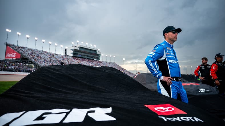 NASCAR Cup Series driver Denny Hamlin waits by his car as rain falls before the Cracker Barrel 400 at Nashville Superspeedway in