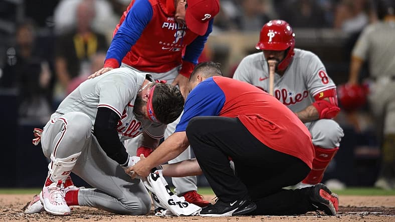 Jun 25, 2022; San Diego, California, USA; Philadelphia Phillies designated hitter Bryce Harper (bottom, left) is checked on by a trainer and interim manager Rob Thomson (top) after being hit by a pitch during the fourth inning against the San Diego Padres at Petco Park. Mandatory Credit: Orlando Ramirez-USA TODAY Sports