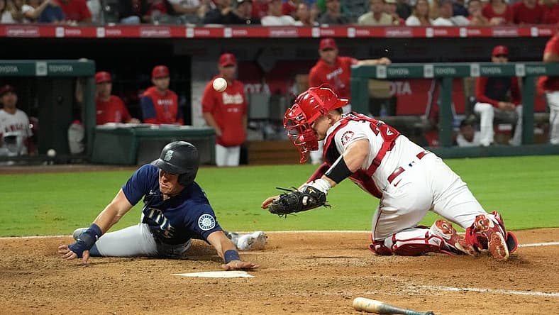Aug 15, 2022; Anaheim, California, USA; Seattle Mariners right fielder Dylan Moore (25) slides into home plate beating a throw to Los Angeles Angels catcher Max Stassi (33) to score in the ninth inning at Angel Stadium. Mandatory Credit: Kirby Lee-USA TODAY Sports