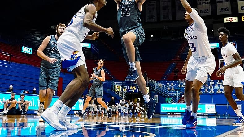 Dec 3, 2020; Lawrence, Kansas, USA; Washburn Ichabods guard Tyler Geiman (12) shoots against Kansas Jayhawks forward Gethro Muscadin (35) and guard Dajuan Harris (3) during the second half at Allen Fieldhouse. Mandatory Credit: Jay Biggerstaff-USA TODAY Sports