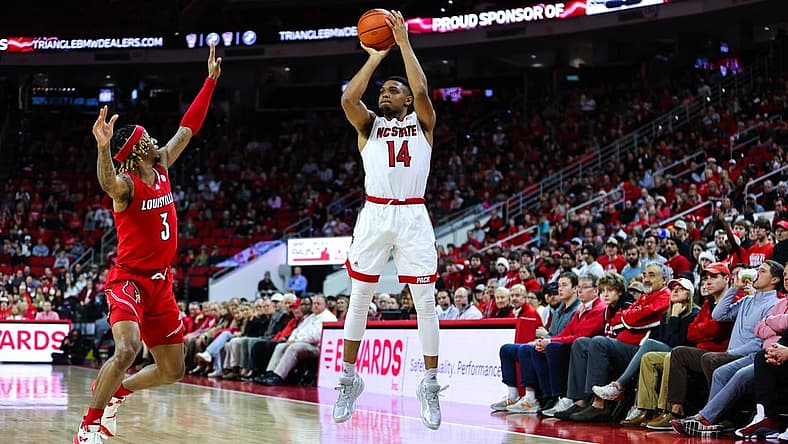 Dec 22, 2022; Raleigh, North Carolina, USA; North Carolina State Wolfpack guard Casey Morsell (14) shoots a three pointer while guard El Ellis (3) tries to block him during the first half against Louisville Cardinals at PNC Arena. Mandatory Credit: Jaylynn Nash-USA TODAY Sports