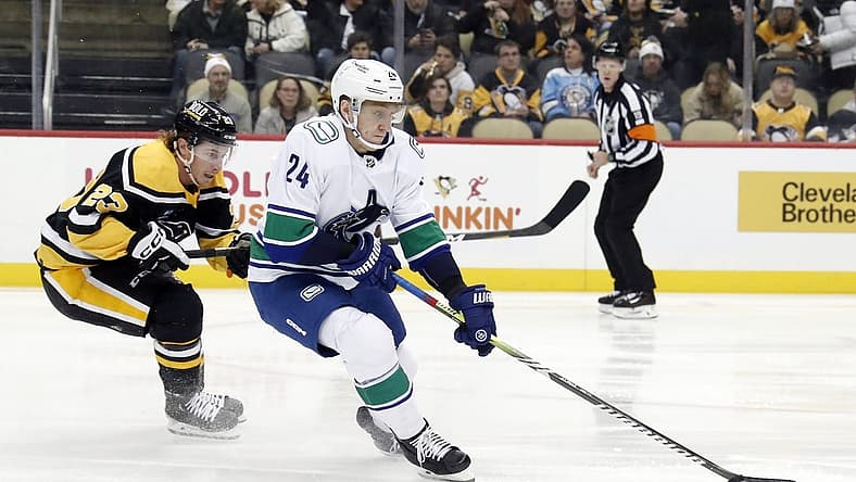 Jan 10, 2023; Pittsburgh, Pennsylvania, USA; Vancouver Canucks defenseman Travis Dermott (24) moves the puck against Pittsburgh Penguins left wing Brock McGinn (23) during the first period at PPG Paints Arena. The Penguins won 5-4. Mandatory Credit: Charles LeClaire-USA TODAY Sports