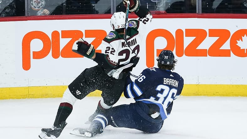 Mar 21, 2023; Winnipeg, Manitoba, CAN; Arizona Coyotes forward Jack McBain (22) battles Winnipeg Jets forward Morgan Barron (36) for the puck during the third period at Canada Life Centre. Mandatory Credit: Terrence Lee-USA TODAY Sports