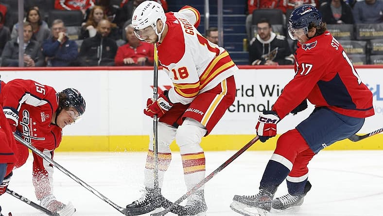 Oct 16, 2023; Washington, District of Columbia, USA; Calgary Flames left wing A.J. Greer (18) battle for the puck with Washington Capitals left wing Sonny Milano (15) and Capitals center Dylan Strome (17) in the second period at Capital One Arena. Mandatory Credit: Geoff Burke-USA TODAY Sports