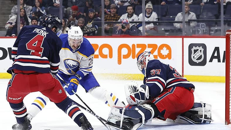 Nov 17, 2023; Winnipeg, Manitoba, CAN; Winnipeg Jets defenseman Neal Pionk (4) and Buffalo Sabres left wing Zemgus Girgensons (28) scramble for a rebound in front of Winnipeg Jets goaltender Connor Hellebuyck (37) in the first period at Canada Life Centre. Mandatory Credit: James Carey Lauder-USA TODAY Sports