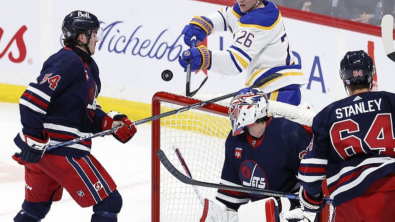 Nov 17, 2023; Winnipeg, Manitoba, CAN; Winnipeg Jets defenseman Dylan Samberg (54) and Buffalo Sabres defenseman Rasmus Dahlin (26) bat at the puck behind Winnipeg Jets goaltender Connor Hellebuyck (37) in the third period at Canada Life Centre. Mandatory Credit: James Carey Lauder-USA TODAY Sports