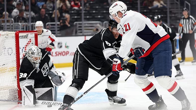 Nov 29, 2023; Los Angeles, California, USA; Washington Capitals center Aliaksei Protas (21) shoots the puck as Los Angeles Kings defenseman Andreas Englund (5) defends and goaltender Cam Talbot (39) protects the goal during the first period at Crypto.com Arena. Mandatory Credit: Kiyoshi Mio-USA TODAY Sports.