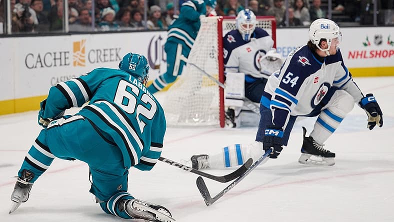 Dec 12, 2023; San Jose, California, USA; San Jose Sharks right wing Kevin Labanc (62) shoots the puck against Winnipeg Jets defenseman Dylan Samberg (54) and goaltender Laurent Brossoit (39) during the second period at SAP Center at San Jose. Mandatory Credit: Robert Edwards-USA TODAY Sports