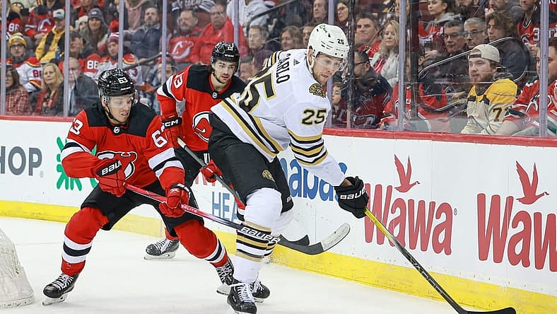 Dec 13, 2023; Newark, New Jersey, USA; Boston Bruins defenseman Brandon Carlo (25) skates with the puck as New Jersey Devils left wing Jesper Bratt (63) and center Nico Hischier (13) defend during the first period at Prudential Center. Mandatory Credit: Vincent Carchietta-USA TODAY Sports