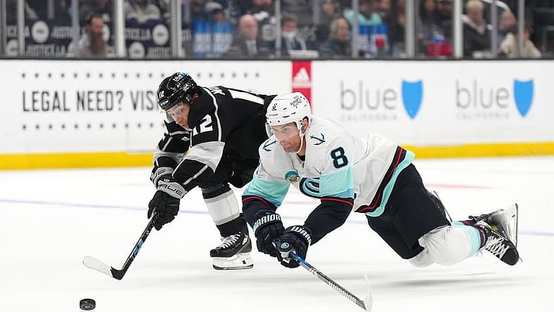 Dec 20, 2023; Los Angeles, California, USA; Seattle Kraken defenseman Brian Dumoulin (8) and LA Kings left wing Trevor Moore (12) reach for the puck in the second period at Crypto.com Arena. Mandatory Credit: Kirby Lee-USA TODAY Sports
