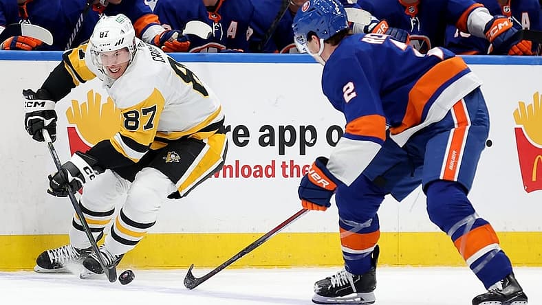 Dec 27, 2023; Elmont, New York, USA; Pittsburgh Penguins center Sidney Crosby (87) controls the puck against New York Islanders defenseman Mike Reilly (2) during the third period at UBS Arena. Mandatory Credit: Brad Penner-USA TODAY Sports