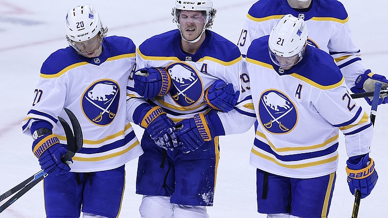 Feb 20, 2021; Newark, New Jersey, USA; Buffalo Sabres defenseman Jake McCabe (19) reacts while being helped off the ice by teammates after suffering an apparent injury during the during the third period against the New Jersey Devils at Prudential Center. Mandatory Credit: Vincent Carchietta-USA TODAY Sports