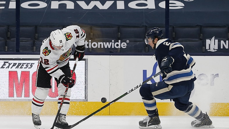 Feb 25, 2021; Columbus, Ohio, USA; Chicago Blackhawks right wing  Alex DeBrincat (12) and Columbus Blue Jackets defenseman Andrew Peeke (2) battle for control of the puck during the second period at Nationwide Arena. Mandatory Credit: Russell LaBounty-USA TODAY Sports
