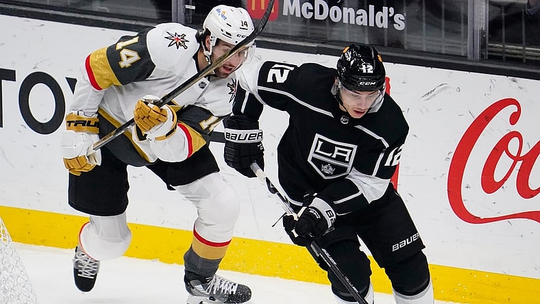 Mar 19, 2021; Los Angeles, California, USA; Los Angeles Kings center Trevor Moore (12) moves the puck away from Vegas Golden Knights defenseman Nicolas Hague (14) during the second period at Staples Center. Mandatory Credit: Robert Hanashiro-USA TODAY Sports