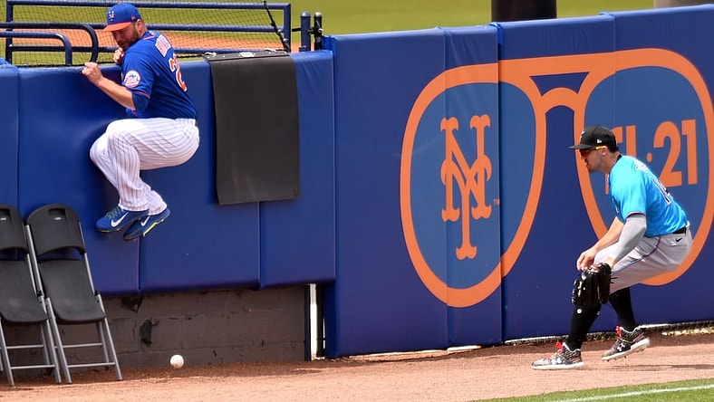 Mar 23, 2021; Port St. Lucie, Florida, USA; New York Mets pitcher Tommy Hunter (L) jumps out of the path of a fair ball as Miami Marlins left fielder Adam Duvall (14) tries to gather the ball in the third inning during a spring training game at Clover Park. Mandatory Credit: Jim Rassol-USA TODAY Sports