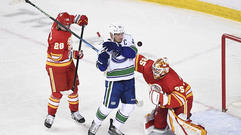 May 13, 2021; Calgary, Alberta, CAN; Vancouver Canucks forward Bo Horvat (53) dodges a shot from near Calgary Flames forward Elias Lindholm (28) and goalie Jacob Markstrom (25) during the first period at Scotiabank Saddledome. Mandatory Credit: Candice Ward-USA TODAY Sports