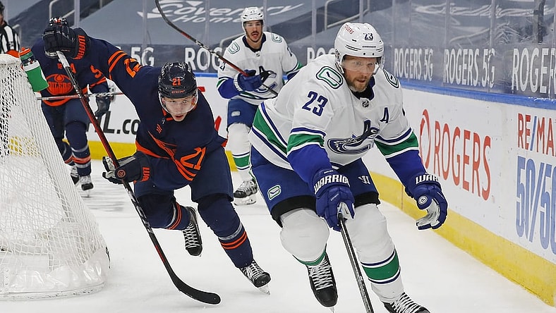 May 15, 2021; Edmonton, Alberta, CAN; Vancouver Canucks defensemen Alex Edler (23) and Edmonton Oilers forward Dominik Kahun (21) chase a loose puck during the third period at Rogers Place. Mandatory Credit: Perry Nelson-USA TODAY Sports