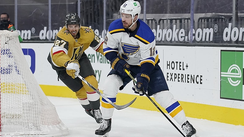 Mar 22, 2021; Las Vegas, Nevada, USA; St. Louis Blues left wing Zach Sanford (12) passes the puck around Vegas Golden Knights defenseman Shea Theodore (27) during the first period at T-Mobile Arena. Mandatory Credit: John Locher /POOL PHOTOS-USA TODAY Sports
