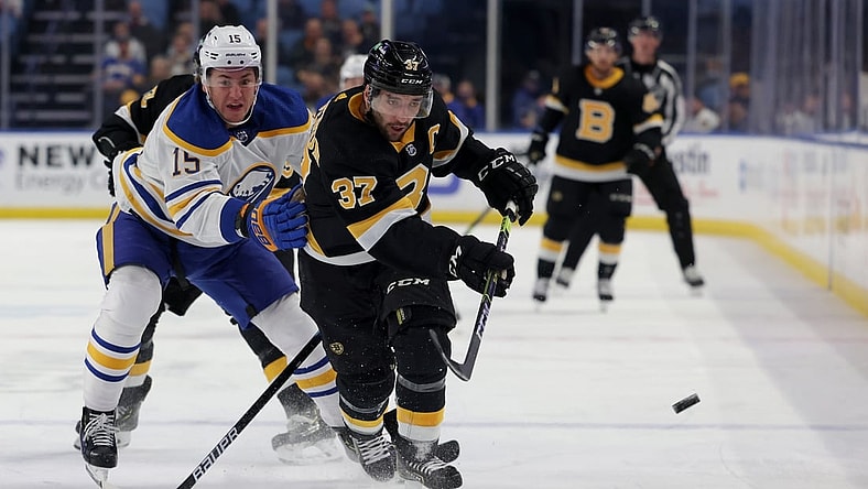 Oct 22, 2021; Buffalo, New York, USA;  Buffalo Sabres left wing John Hayden (15) tries to defend as Boston Bruins center Patrice Bergeron (37) shoots the puck along the boards during the first period at KeyBank Center. Mandatory Credit: Timothy T. Ludwig-USA TODAY Sports