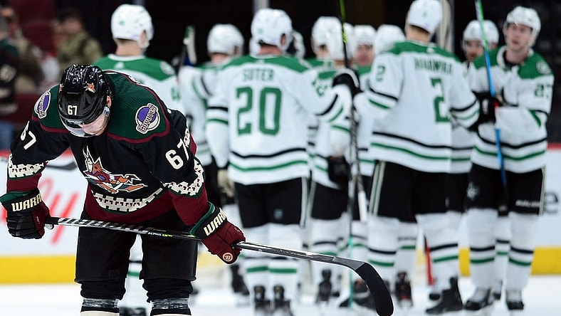 Nov 27, 2021; Glendale, Arizona, USA; Arizona Coyotes left wing Lawson Crouse (67) leaves the ice as Dallas Stars players celebrate their victory after the game at Gila River Arena. Mandatory Credit: Joe Camporeale-USA TODAY Sports