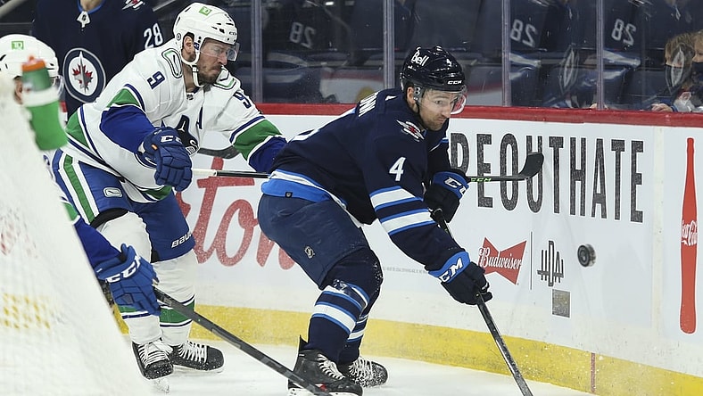 Jan 27, 2022; Winnipeg, Manitoba, CAN;  Winnipeg Jets defenseman Neal Pionk (4) and Vancouver Canucks forward J.T. Miller (9) battle for the put during the first period at Canada Life Centre. Mandatory Credit: Terrence Lee-USA TODAY Sports